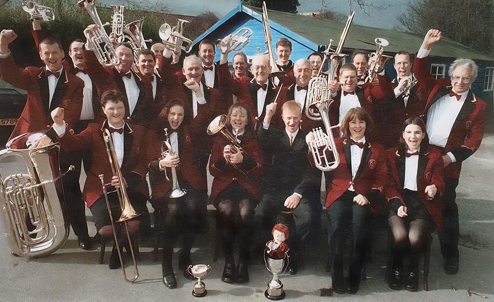 An earlier Knottingley Silver Band lineup in burgundy jackets, celebrating with instruments and trophies